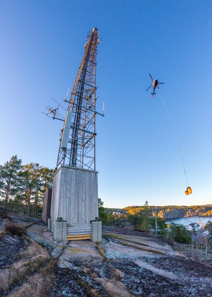 Photo of a helicopter flying next to a telecom mast.
